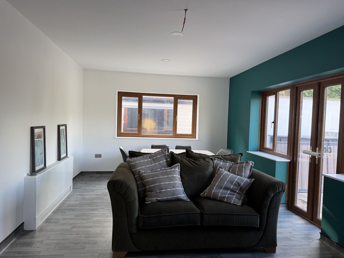 Living room at Balan House with a deep green feature wall, oak-framed windows and French doors to the garden